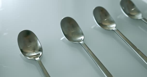 Extreme close-up, detailed. large and small stainless steel spoons on a white glossy surface — Video