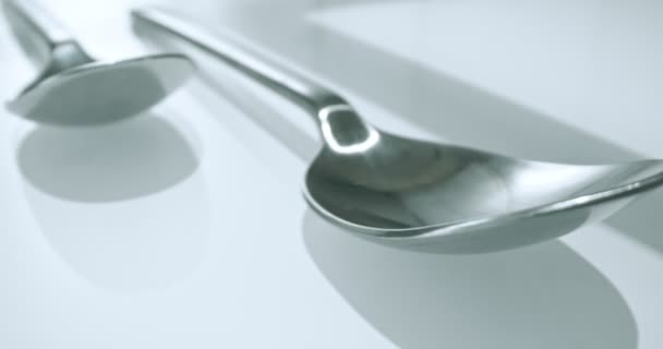 Extreme close-up, detailed. large and small stainless steel spoons on a white glossy surface — Video Stock