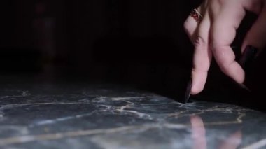 close-up, female fingers with long black nails step on a black reflective surface