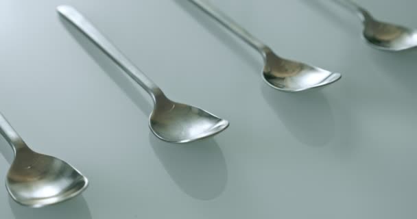 Extreme close-up, detailed. large and small stainless steel spoons on a white glossy surface — Stockvideo