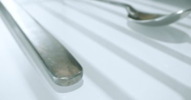 extreme close-up, detailed. large and small stainless steel spoons on a white glossy surface