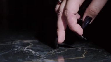 close-up, female fingers with long black nails step on a black reflective surface