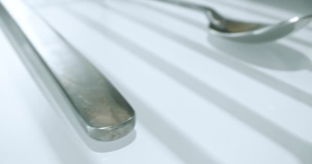 Extreme close-up, detailed. large and small stainless steel spoons on a white glossy surface — Αρχείο Βίντεο