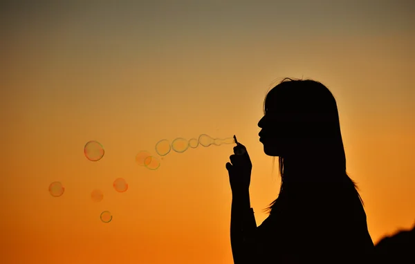 Kız siluet, günbatımında kabarcıklar üfleme.