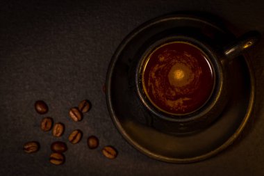 Siyah killi kahve fincanı, çay tabağı ve koyu arkaplanda dağınık kahve çekirdekleri.