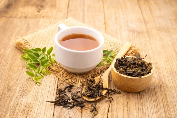 White cup of hot tea and dry tea leaf on wooden table background