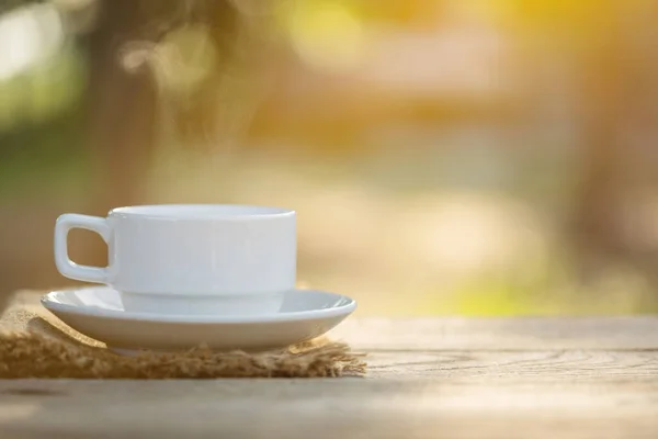 朝の陽射しとボケを背景に屋外の木製テーブルの上にコーヒーとコーヒー豆のカップを閉じます — ストック写真