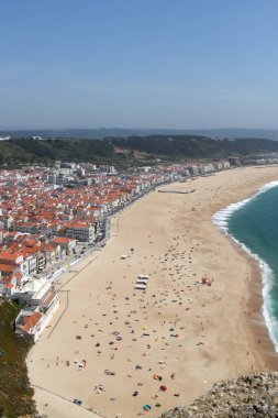 Güzel kumlu sahil manzarası ve Portekiz 'deki Nazare kayalıklarından Atlantik okyanus kıyısında kil kil kiremitli çatıları olan beyaz evler.