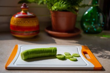 Mutfaktaki kesme tahtasının üzerinde soyulmuş, dilimlenmiş salatalık. Pencereden güneş ışığı akıyor. Sağlıklı kahvaltı. İsrail kahvaltısı.