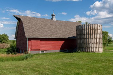 Kahverengi kiremitli çatılı kırmızı ahır ve Minnesota, ABD kırsalındaki bir çiftlikte eski silo..
