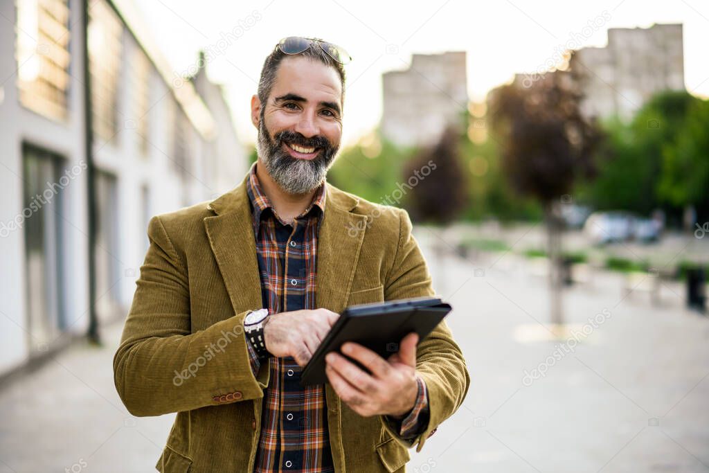 Portrait of modern businessman  with beard using digital tablet while  standing in on the city street.