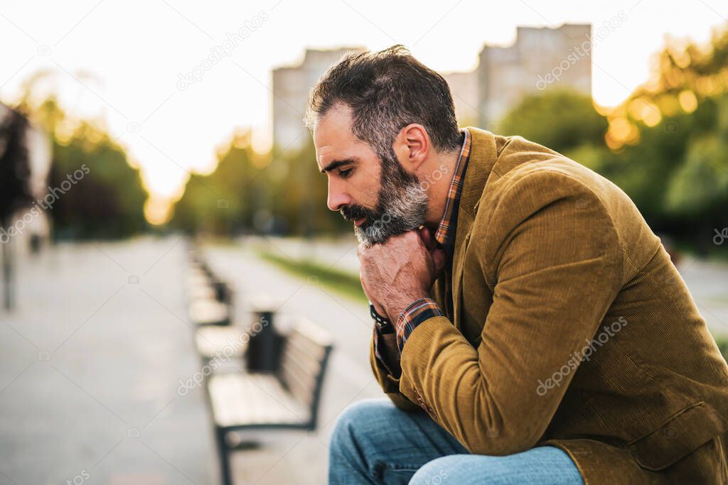 Depressed businessman  with beard sitting on the bench in the city.