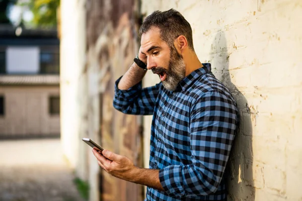 Geschockter Geschäftsmann Mit Bart Blickt Vor Wand Auf Sein Handy — Stockfoto