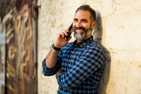 壁の屋外の前に立っている間 携帯電話を使用して髭を生やした現代のビジネスマン — ストック写真