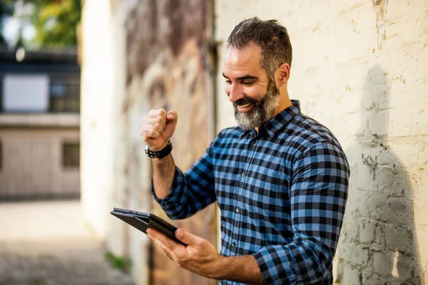 Aufgeregt Moderner Geschäftsmann Mit Bart Mit Digitalem Tablet Vor Backsteinmauer — Stockfoto