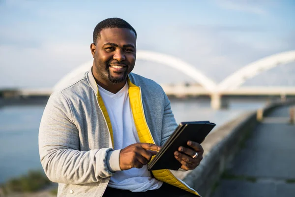 Modern Siyah Adam Nehir Kenarında Otururken Dijital Tablet Kullanıyor — Stok fotoğraf
