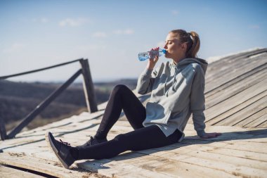 Sportif kadın doğadaki eski köprüde otururken egzersizden sonra dinleniyor ve su içiyor..