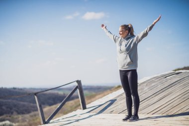 Kollarını açarak eski köprüde duran ve doğayı seven sportif bir kadın..