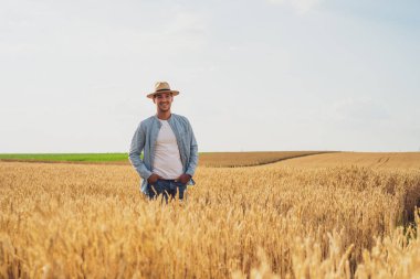 Happy farmer is standing in his growing wheat field.