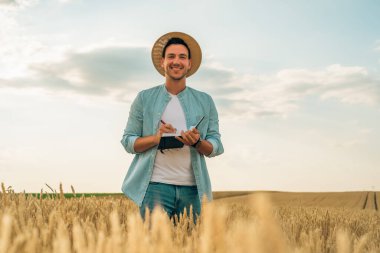 Mutlu çiftçi buğday tarlasında dikilirken notlar yazıyor..