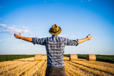 Başarılı hasattan sonra saman balyalarının yanında duran kollarını açmış mutlu çiftçi..