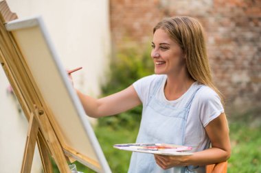 Woman enjoys painting on canvas outdoor.
