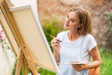 Woman enjoys painting on canvas outdoor.