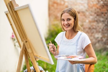 Woman enjoys painting on canvas outdoor.