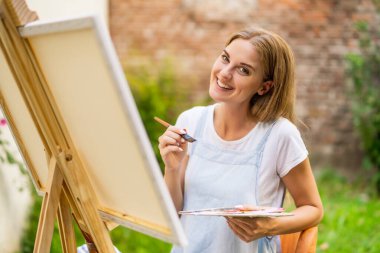 Woman enjoys painting on canvas outdoor.