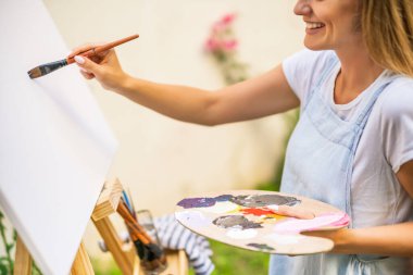 Woman enjoys painting on canvas outdoor.