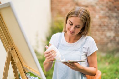 Woman enjoys painting on canvas outdoor.