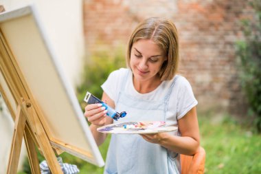 Woman enjoys painting on canvas outdoor.