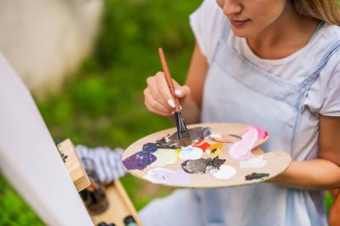 Woman enjoys painting on canvas outdoor.