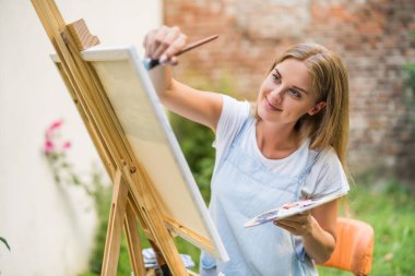 Woman enjoys painting on canvas outdoor.