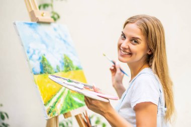 Woman enjoys  painting on canvas outdoor.