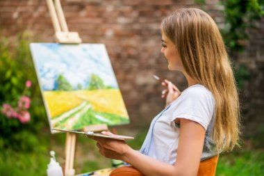 Woman enjoys painting on canvas outdoor.