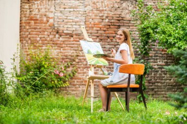 Woman enjoys  painting on canvas outdoor.