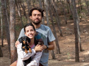 Mutlu genç beyaz çift sonbaharda ormanda Minyatür Dachshund köpekleri ile gülümsüyor.