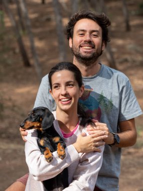 Mutlu genç beyaz çift sonbaharda ormanda Minyatür Dachshund köpekleri ile gülümsüyor.