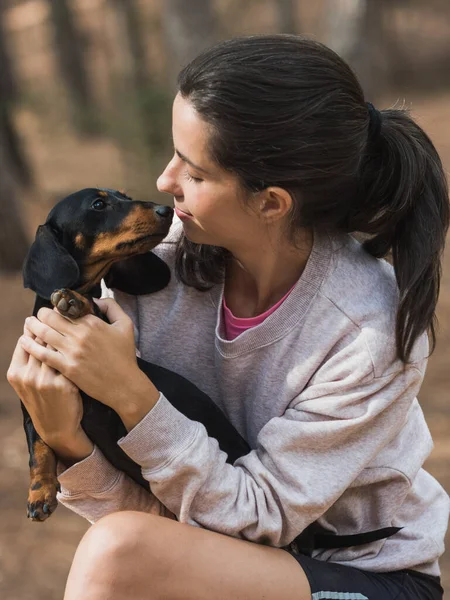 Genç beyaz bir kadın ormanda siyah, pürüzsüz saçlı, minyatür bir dachshund arıyor.