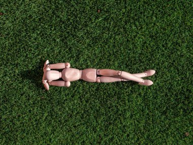 İnsan ahşap bebek çimenlerin üzerinde uzanmış, güneşleniyor.