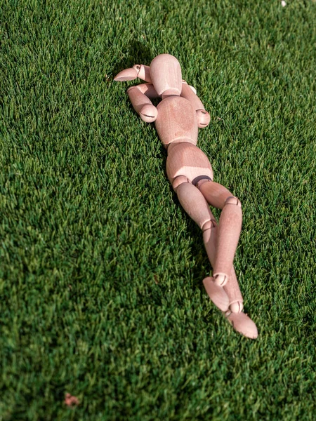 İnsan ahşap bebek çimenlerin üzerinde uzanmış, güneşleniyor.