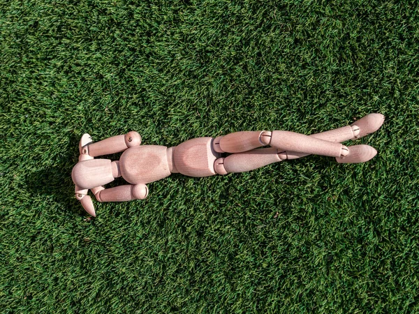 İnsan ahşap bebek çimenlerin üzerinde uzanmış, güneşleniyor.