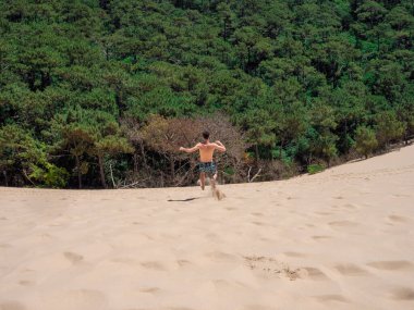 Young caucasian man walking and jumping on the sand in Dune of Pilat in Arcachon France
