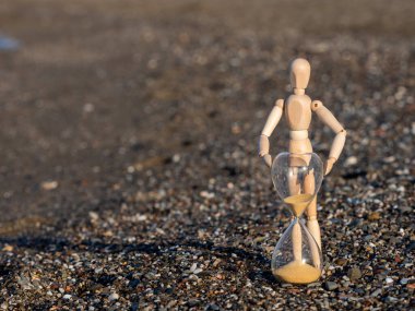 Human Wooden stick figure next to hourglass on the beach at the seashore