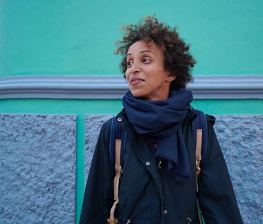 Siyah bir kadının portresi günlük kıyafetler içinde ve mavi ve yeşil duvar arkasında kısa kıvırcık saçlar.