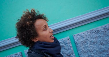 Siyah bir kadının portresi günlük kıyafetler içinde ve mavi ve yeşil duvar arkasında kısa kıvırcık saçlar.