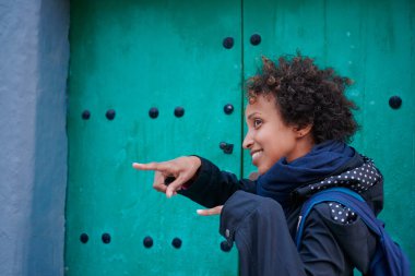 Gündelik giysiler içinde gülümseyen siyah bir kadın portresi ve iki eli kapının önünde olan kıvırcık saçlar.