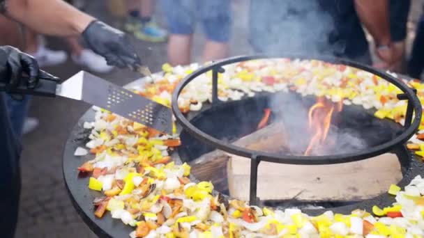 Zwarte ronde BBQ roker op traditionele barbecue festival buiten, chef-kok in handschoenen roosteren gesneden tomaten, aubergines, ui, rode en gele paprika 's op bbq rooster en draaien rond met metaal — Stockvideo