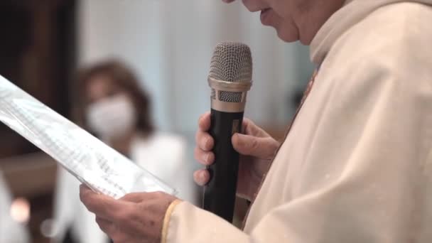 Итальянский местный священник, читающий проповеди из листовой бумаги и пользующийся микрофоном, старший пастор традиционной итальянской католической церкви проводит ритуальную проповедь во время свадьбы или крещения — стоковое видео